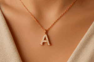 Raudono (rose) aukso grandinėlė su deimantais inkrustuota „A“ raide elegantiškai guli ant moters kaklo